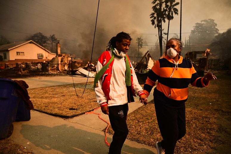 Dos personas tomadas de la mano mientras caminan por una calle suburbana con el humo de los incendios forestales en el fondo