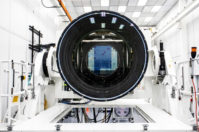 Una vista de la enorme abertura de la cámara LSST. Tiene forma de una gran dona negra, con reflejos de la luz del techo que revelan la presencia de lentes de vidrio.